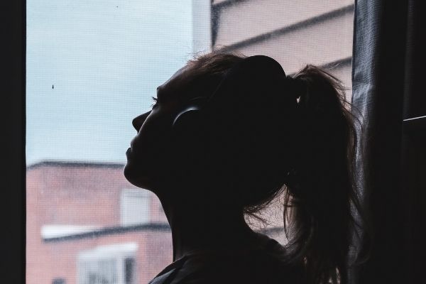 A young woman wearing headphones looks out of her window